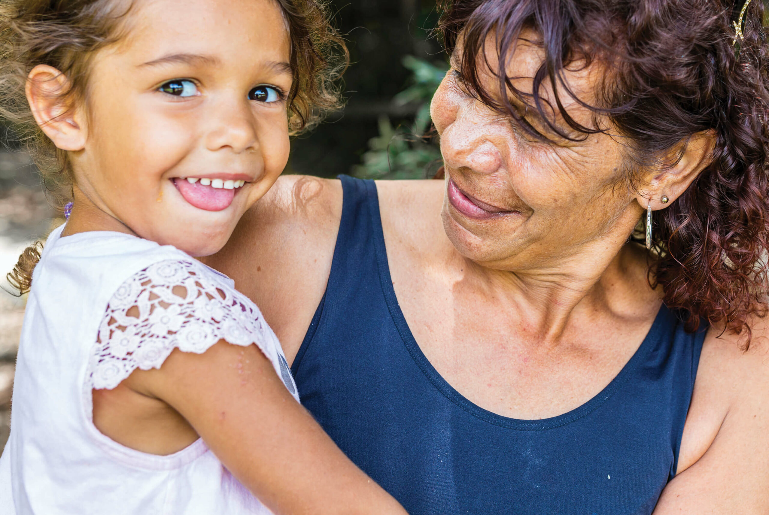 Smiling grandmother holding and looking at happy granddaughter.