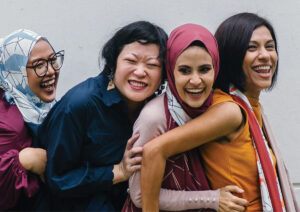 Row of four women in congo line smiling.