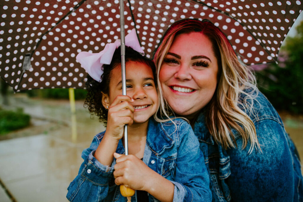 Mother and child standing underneath an umbrella smiling.